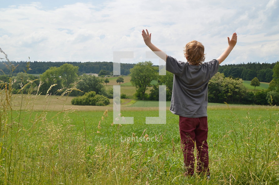 child with raised arms in adoration outdoors at a meadow. 
