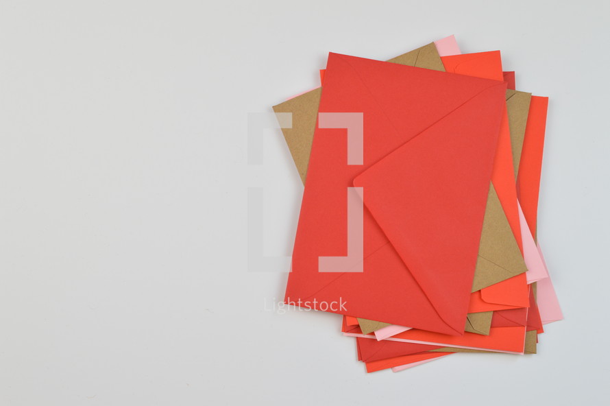 stacked envelope - pile of red, pink and brown envelopes on white background with copy space to the left  