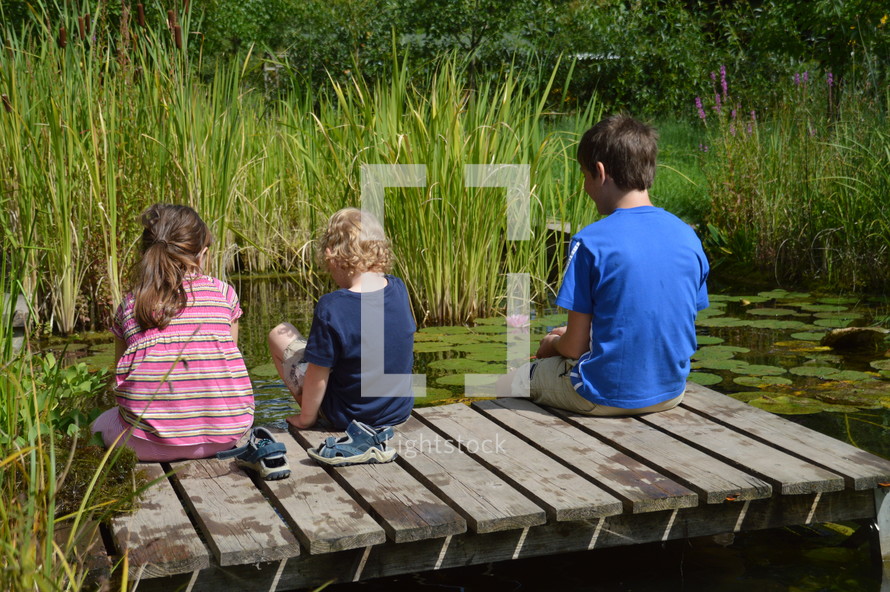 children sitting on a dock on a pond 