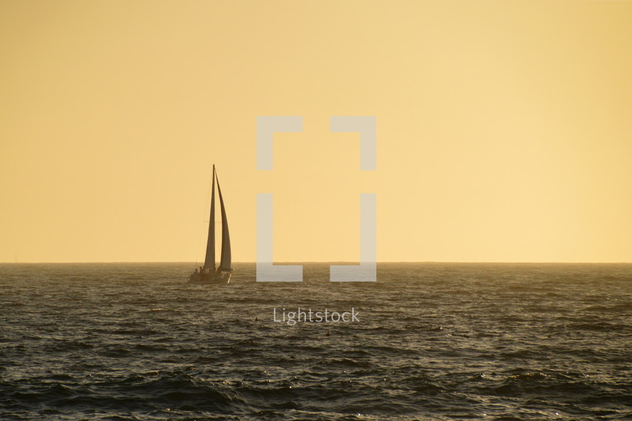 little sailboat sailing on the wide ocean in the yellow light of sundown. 
