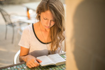 a woman sitting at an outdoor table at a restaurant while reading a Bible 