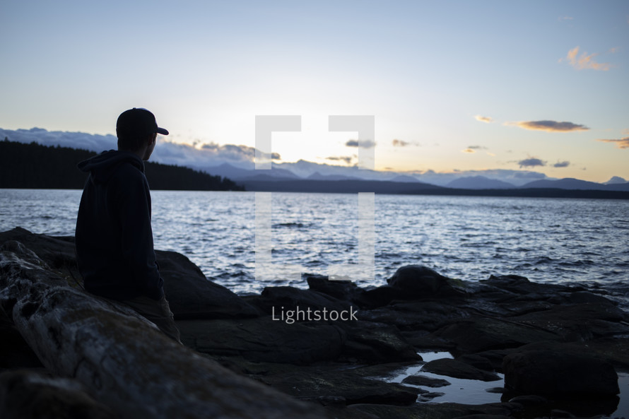 silhouette of a man sitting along a shore 