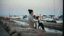 Woman with her dog sitting on rocks by boats