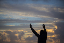 silhouette with raised hands on a beach at sunset 