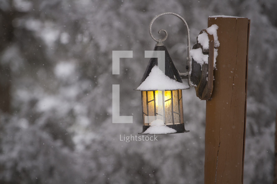 A snow covered lantern on a wooden post.