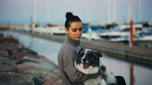 Woman with her dog sitting on rocks by boats