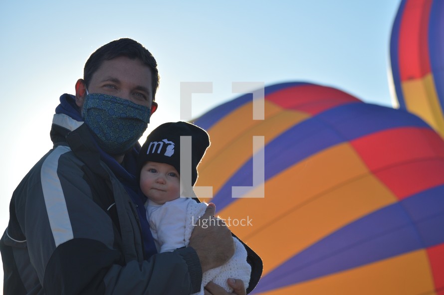 a father holding an infant and a hot air balloon 
