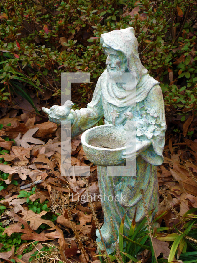 A statue of Patron Saint Francis ministering to birds while surrounded by fallen leaves in the fall of Virginia. 