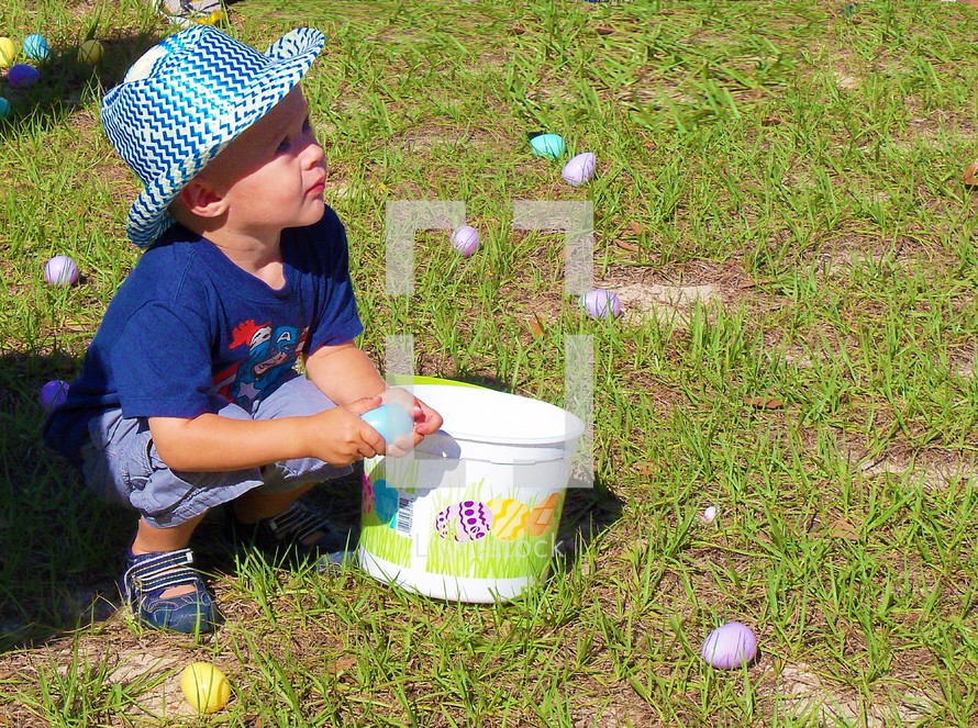 A young boy wearing a hat collects Easter Eggs at an outdoor Church Easter Egg Hunt for children at Easter Time. 