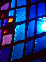 Sun pours through a blue, purple and red stained glass window adding light and color to a prayer chapel during morning worship time. 