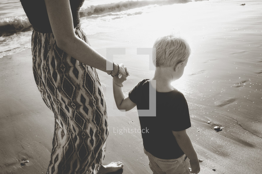 a mother and son walking on a beach holding hands 
