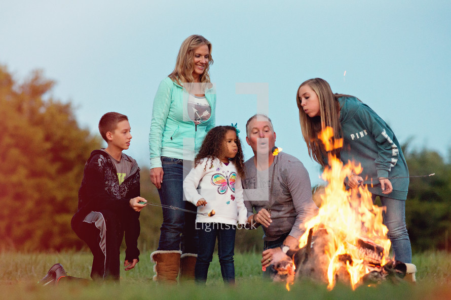 a family sitting by a campfire roasting marshmallows 