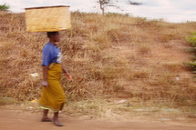 A woman carrying a basket on her head. 