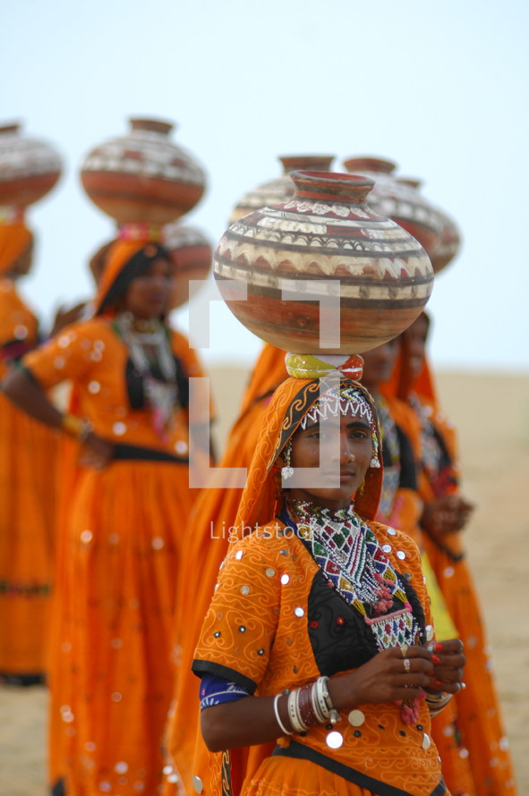 female Hindu women walking with water jugs on their heads 