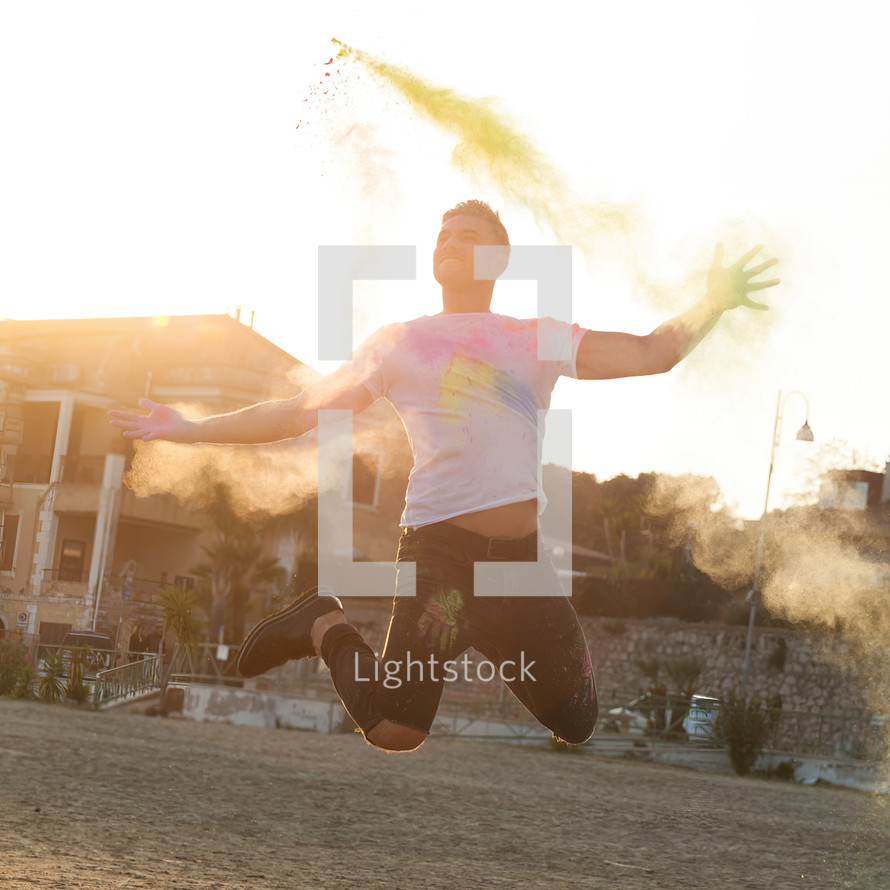 Portrait at sunset of a young man jumping with energy and colored powder.
