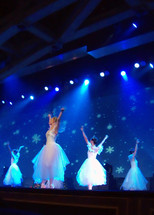 A group of ballet dancers performing the nutcracker ballet from the Ukraine at a local church during Christmas time, dancing against a blue background with snow flakes and stage spot lights.  
