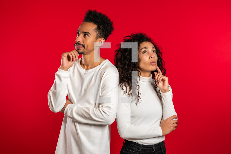 Portrait of young thinking pondering couple on red studio background. Man and woman look in different directions and everyone thinks about his problem