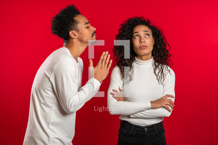 Cute african young man begging his girlfriend or wife about something over red background