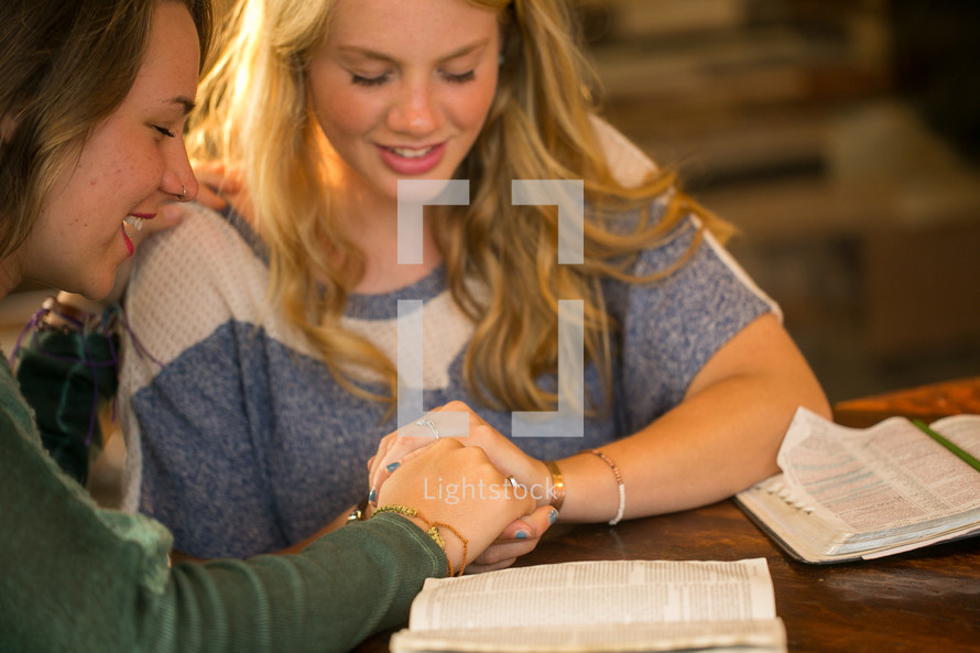 women holding hands in prayer over a Bible 