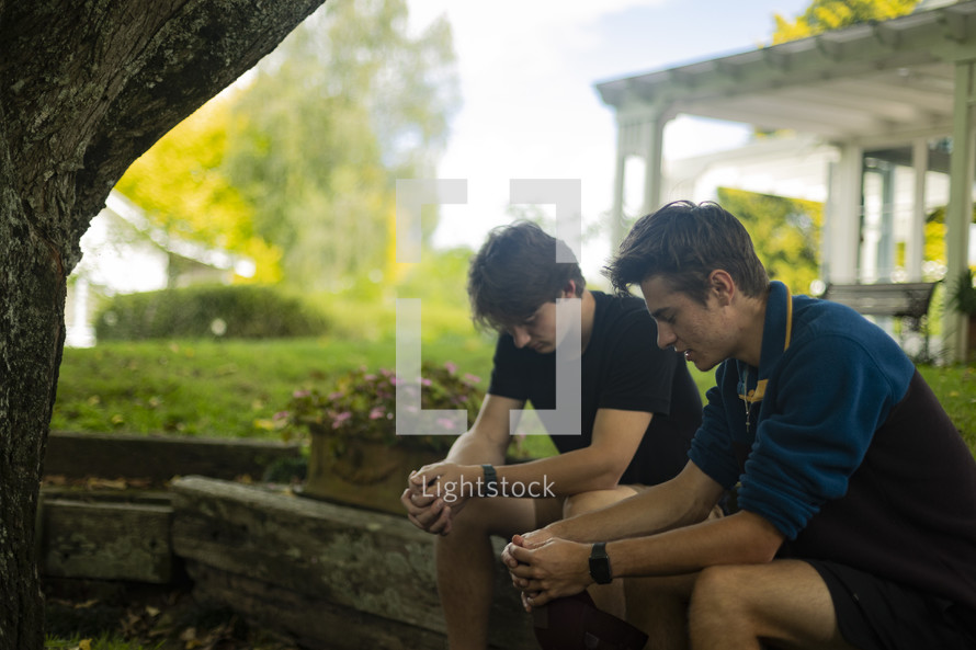 two young men sitting together praying in a beautiful setting