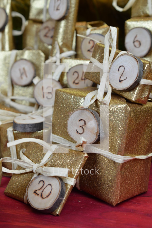 advent calendar with twenty four golden presents on red wood with the numbers burned into round wood pieces and the numbers 20, 3 and 2 up close