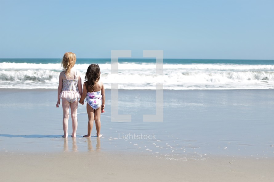 sisters in bathing suits holding hands on a beach 