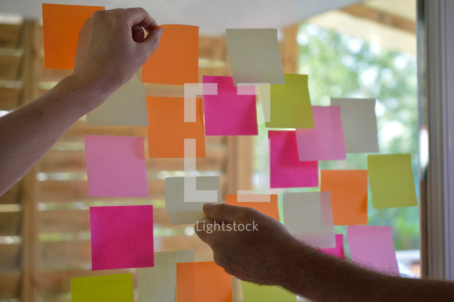 hands sticking colorful bright notepads on glass wall