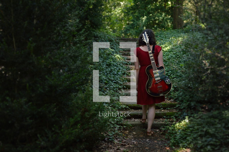a woman in a red dress with an electric guitar walking through the dark woods 