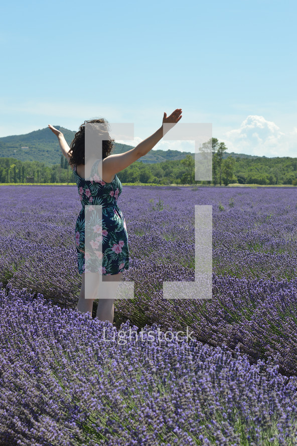 a woman standing in a field of lavender with arms raised in praise 