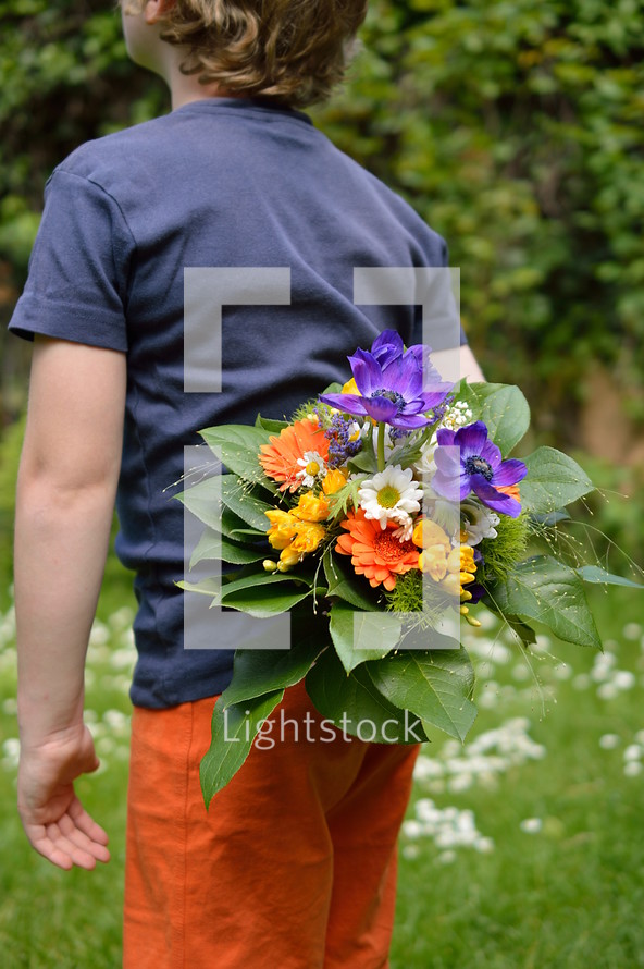 a child holding a bouquet of flowers behind his back 