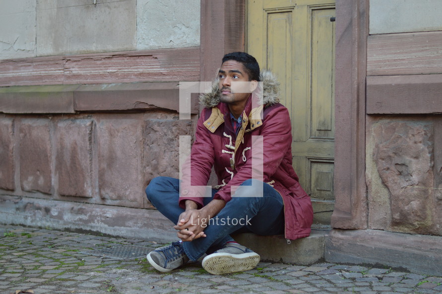 man in a coat sitting in front of a door 