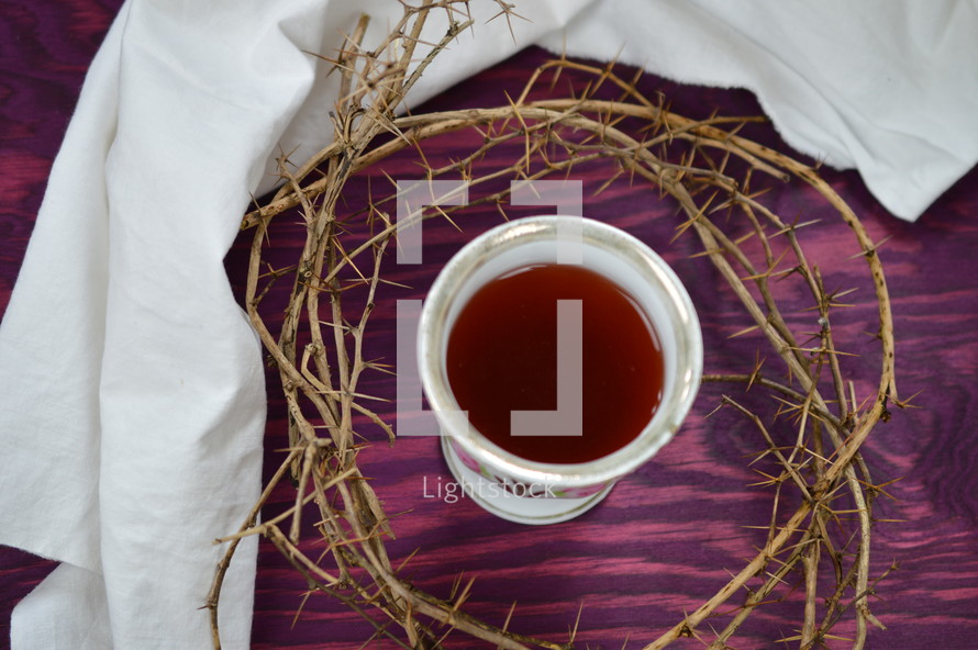 crown of thorns, a piece of cloth and a cup of red wine on purple wood