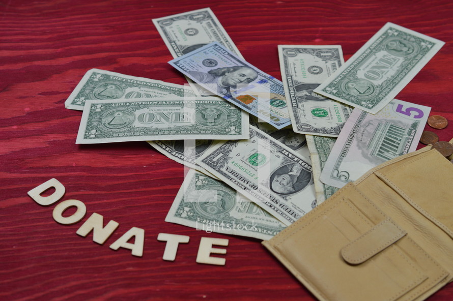 money spilling out from a wallet on a red wooden table with the word donate in wooden letters