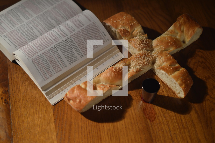 open Bible, bread in the shape of a cross, and cup of communion wine 