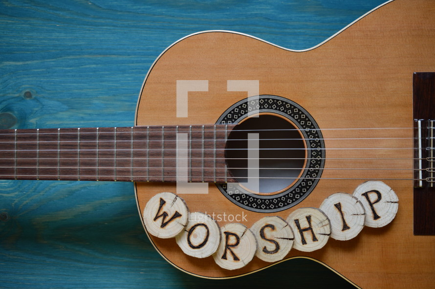 guitar on teal wooden background with wood pieces on it lettering the word: WORSHIP