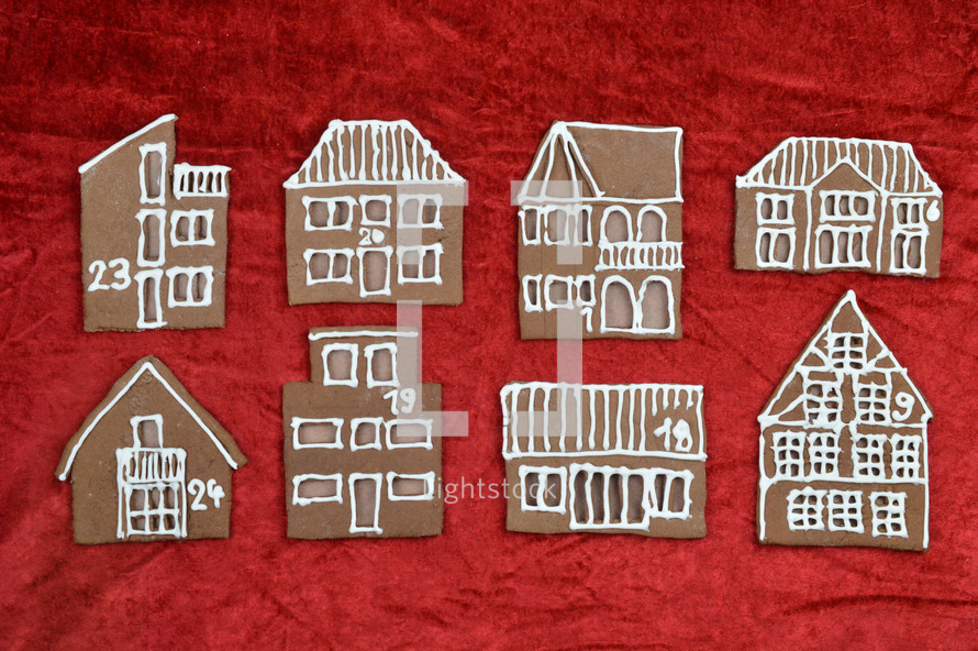 eight different self baked gingerbread house fronts with numbers on them on red velvet as part of an advent calendar