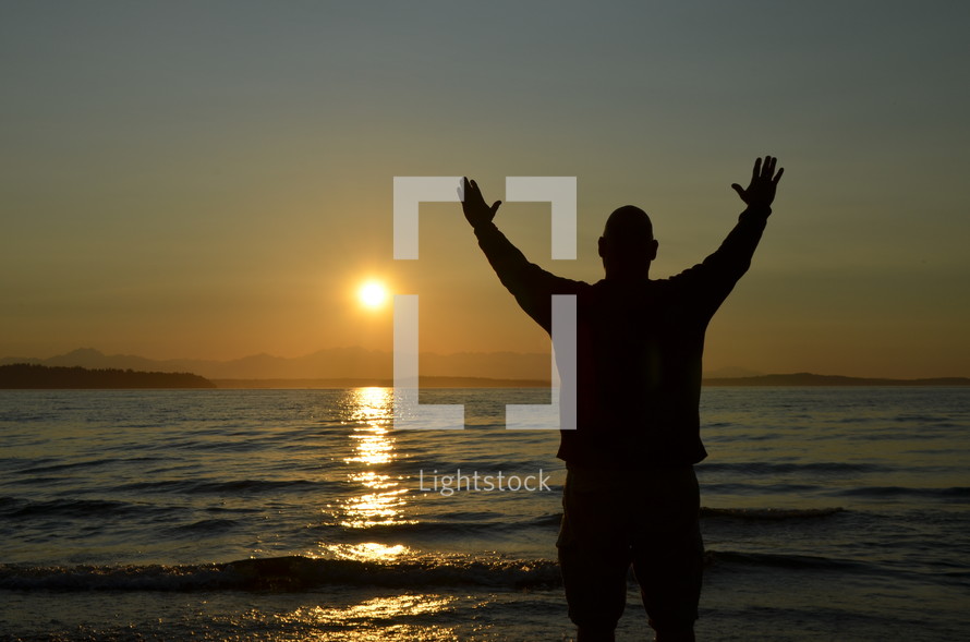 silhouette of a man with hands raised in worship on a beach 