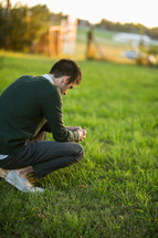 a man squatting in grass praying 