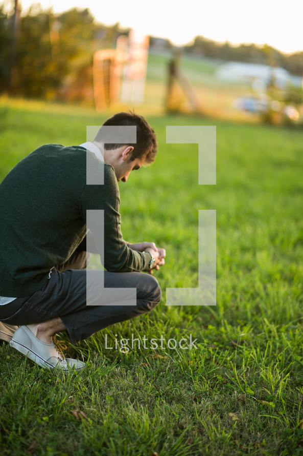 a man squatting in grass praying 