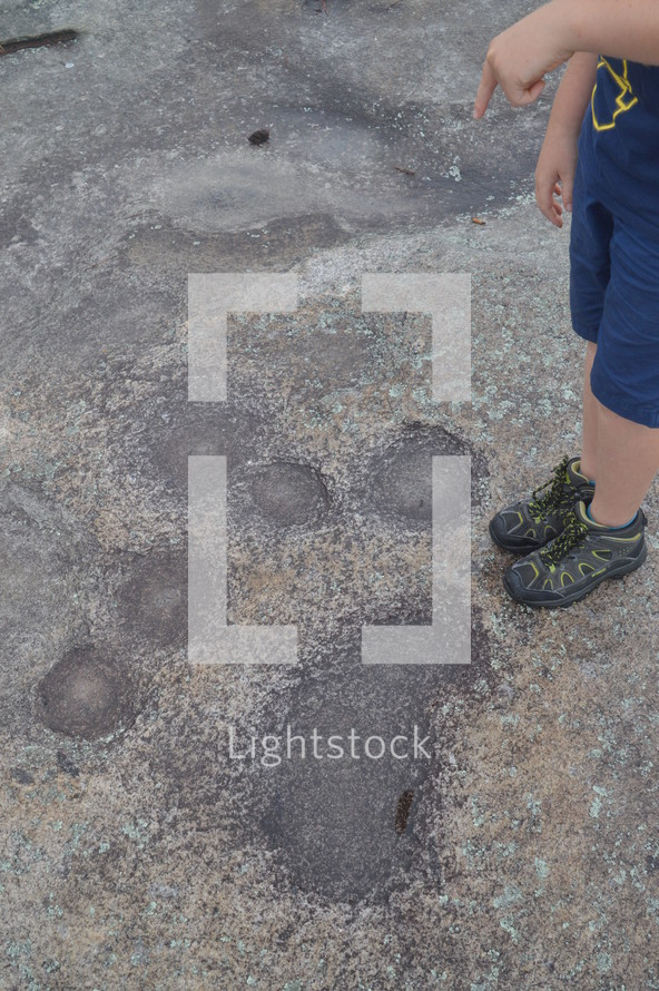 boy standing next to spots on a rock surface 