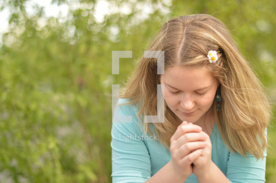Young blond woman praying outdoors. 