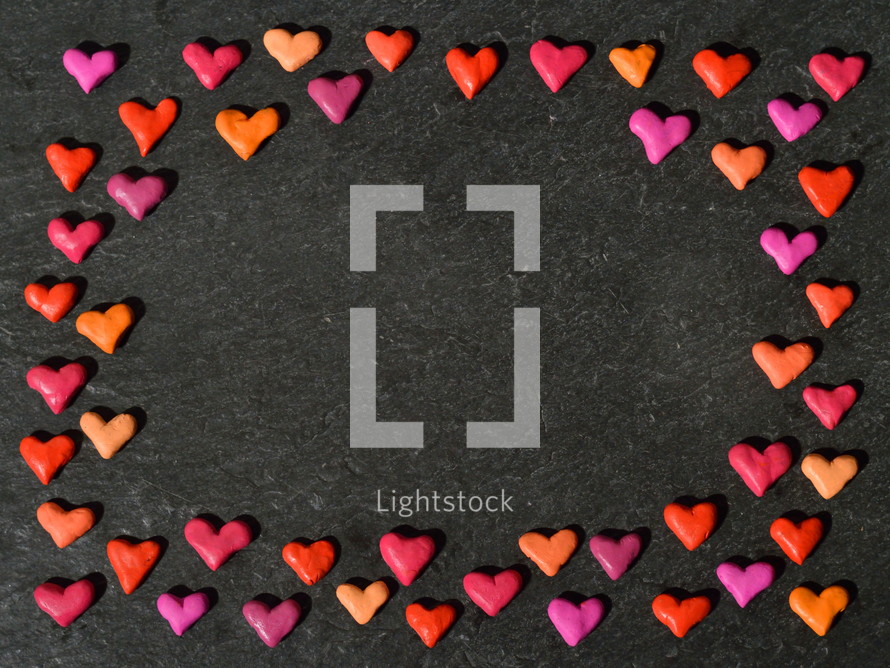 colorful clay hearts frame on a black slate background 