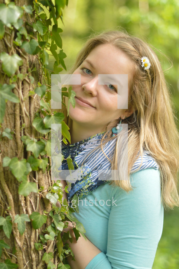 blond woman standing next to a tree and smiling. 
