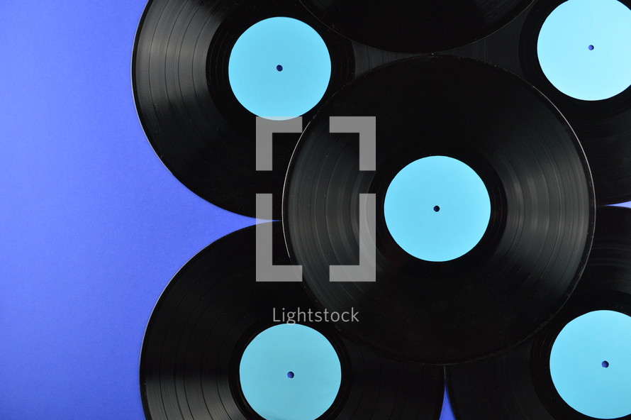pile of old black vinyl records with blank cyan labels on blue background
