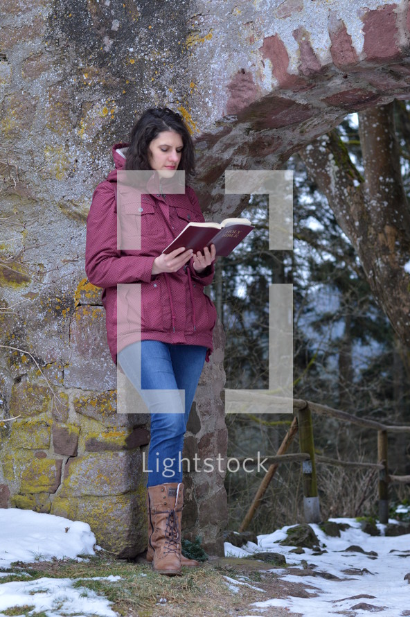 a woman standing outdoors reading a Bible 