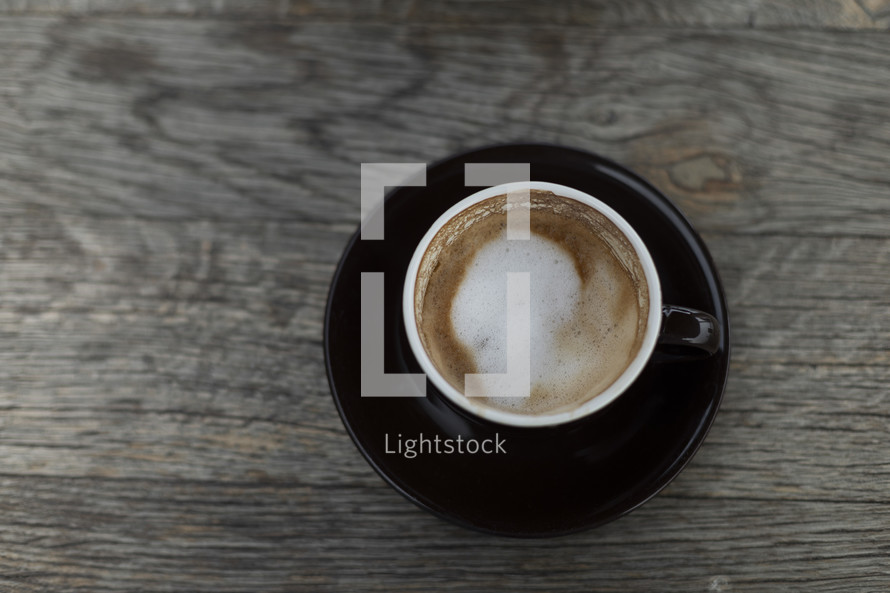 Coffee with foam in black mug on wooden table