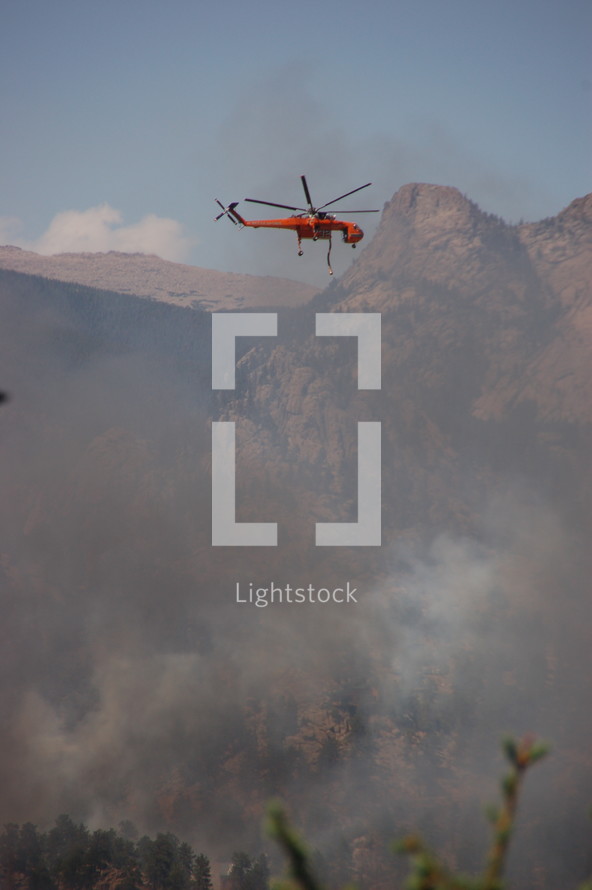 a helicopter with buckets flying over a forest fire 