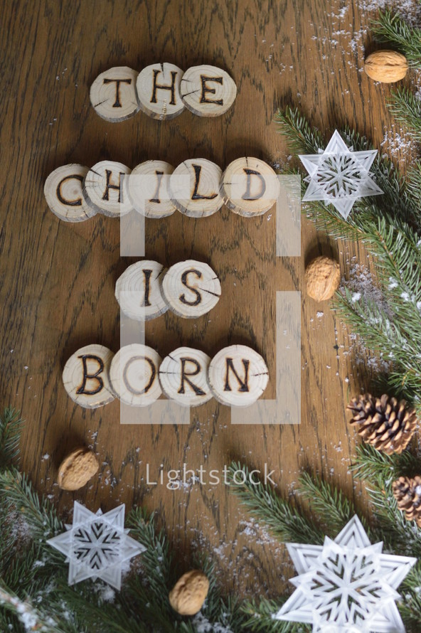 star ornaments, pine cones, snow, pine boughs and the words THE CHILD IS BORN on wooden slices