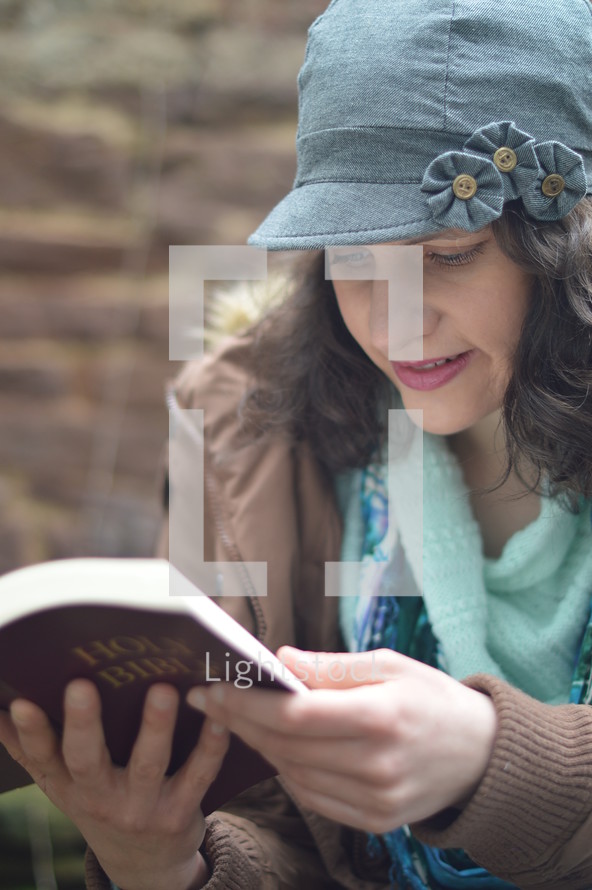 a woman in a hat reading a Bible outdoors 