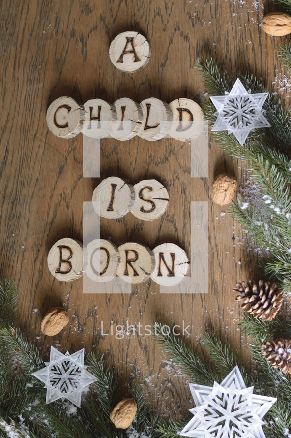 star ornaments, pine cones, snow, pine boughs and the words A CHILD IS BORN on wooden slices
